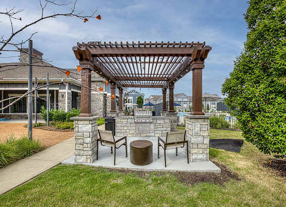 A wooden pergola with a bench and table is in the foreground of a residential area.
