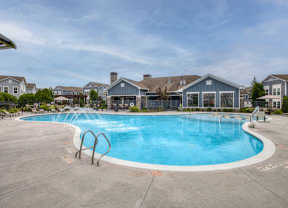A large outdoor swimming pool surrounded by a concrete patio and residential buildings.