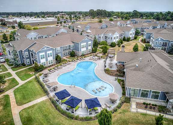 A large swimming pool surrounded by blue umbrellas and lounge chairs in a residential area.