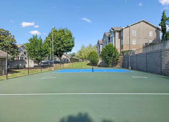 A tennis court surrounded by a fence and apartment buildings.