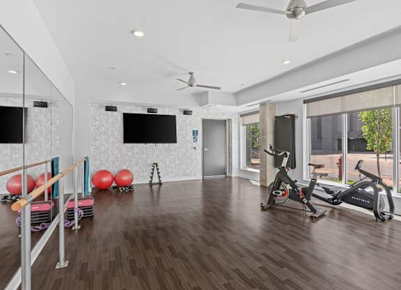A spacious room with a wooden floor, a mirror, a fan, and exercise equipment.