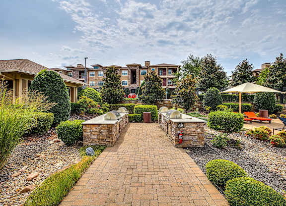 A brick pathway leads to a building with a patio and a fire pit.