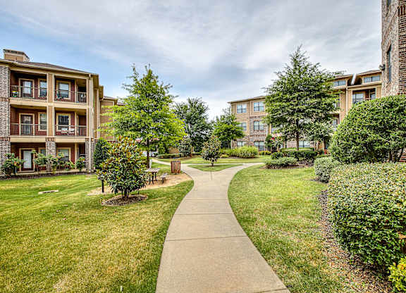 A pathway leads through a grassy area between two apartment buildings.