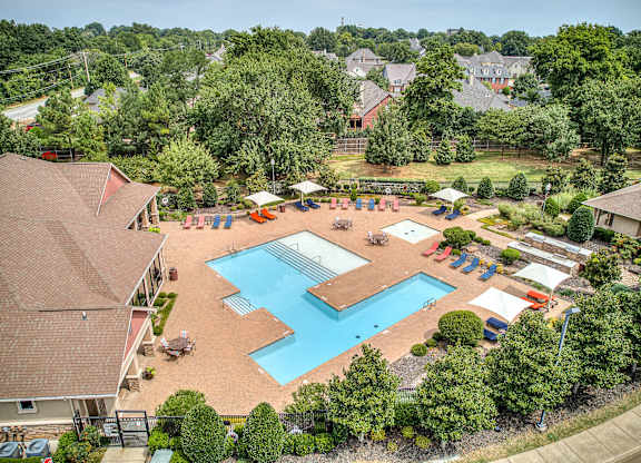 A large swimming pool surrounded by trees and a playground.