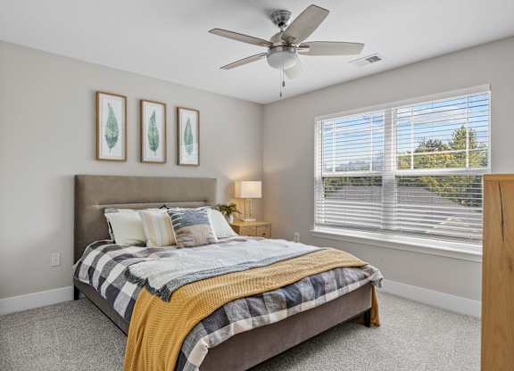 A bedroom with a bed, a ceiling fan, and two framed pictures on the wall.