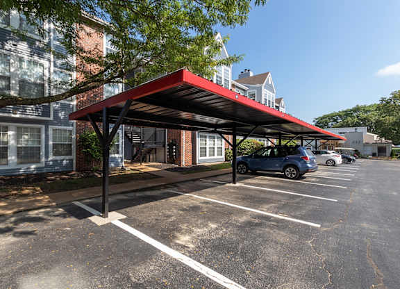 A view of a parking lot near a residence entrance with a red carport canopy over several vehicles.