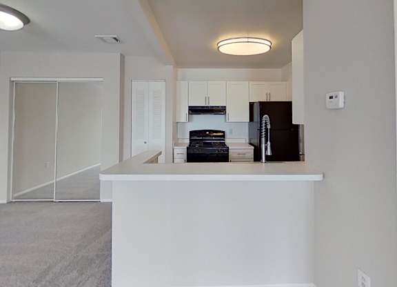 A kitchen area with a black fridge and white countertop.