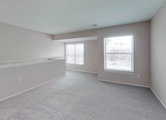 A spacious room with carpeted flooring and two large windows.