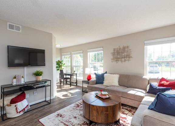 A living room with three windows, a couch, a coffee table, and a television.