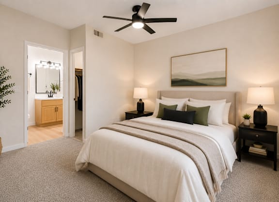 A bedroom with a large bed, a ceiling fan, and a potted plant.