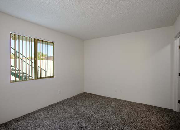 A room with a carpeted floor and a window with bars.