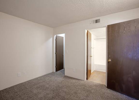A room with a carpeted floor and two doors, one of which is open.