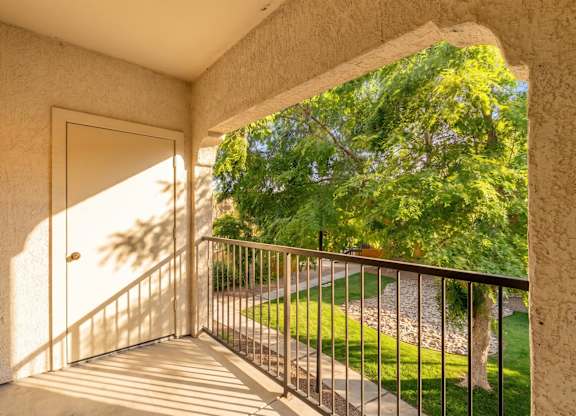 A balcony with a metal railing and a view of a green lawn and trees.