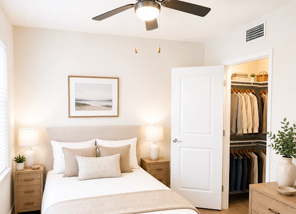 A bedroom with a large bed, a ceiling fan, and a closet with clothes.