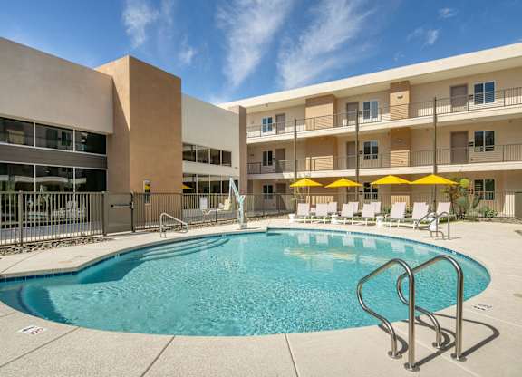 A swimming pool in front of a building with yellow umbrellas.