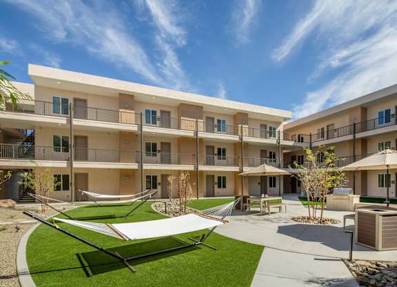 A sunny day at a modern apartment complex with a green lawn and a white shade sail.