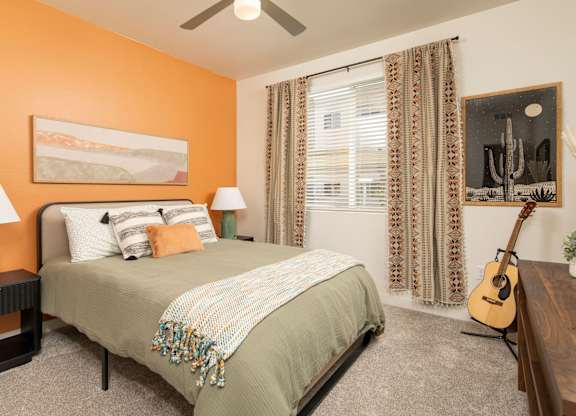 A bedroom with a bed, two lamps, a guitar, and a painting on the wall.