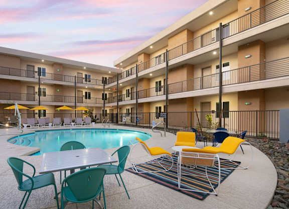 A pool area with chairs and tables is surrounded by apartment buildings.