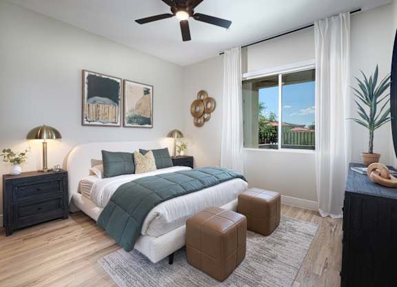 A bedroom with a large bed, a ceiling fan, and a window with a view of the outdoors.