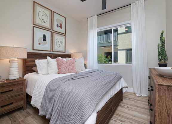 A bedroom with a bed, nightstand, and a window with white curtains.