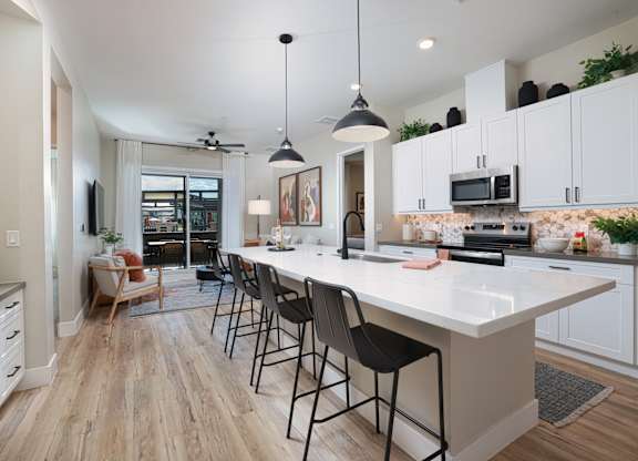 A modern kitchen with a white island and black chairs.