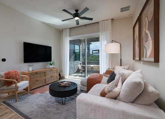 A living room with a white couch, a wooden chair, a black coffee table, and a flat-screen TV mounted on the wall.