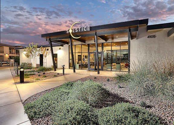 The image shows the front of a building named Solstice with a modern design, featuring a large glass entrance and a landscaped area in front.