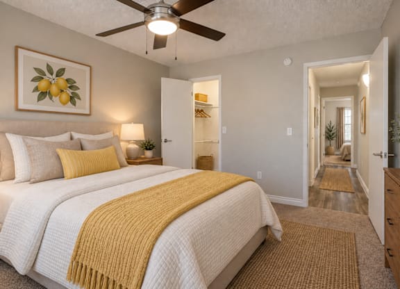 A bedroom with a bed, a ceiling fan, and a painting of lemons on the wall.
