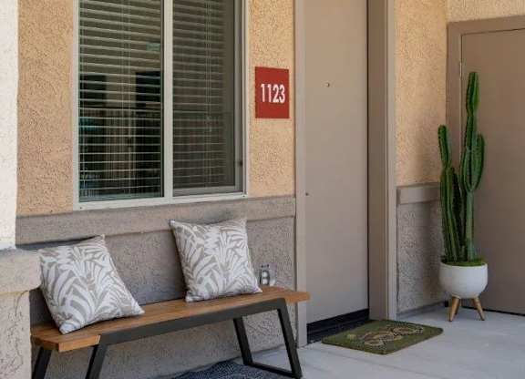 A bench with two cushions sits in front of a window with blinds.