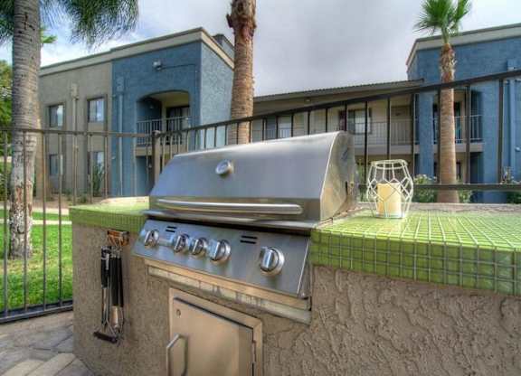 A silver barbecue grill with a green tiled area in front of it.