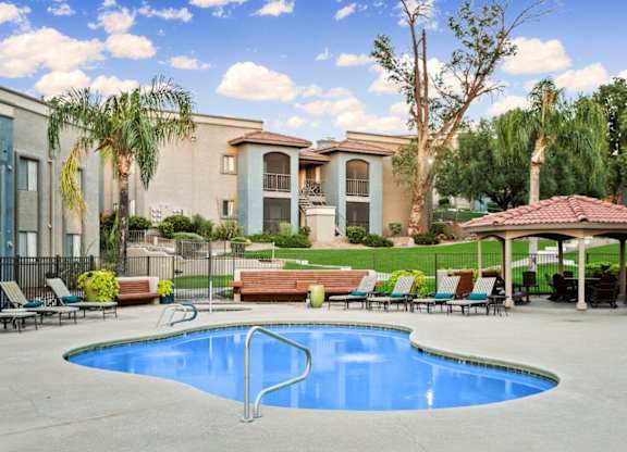 A swimming pool in front of a house with a patio and trees.