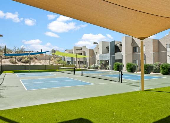 A tennis court is surrounded by a grassy area and a building in the background.