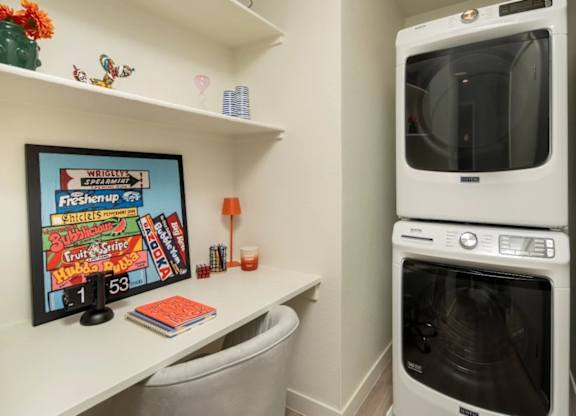 A white washing machine is in a small laundry room with a framed sign on the wall.