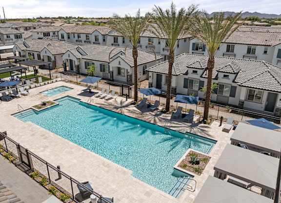 A swimming pool surrounded by palm trees and lounge chairs in a residential area.