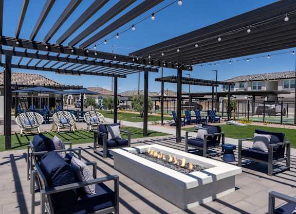 A patio with a fire pit and chairs under a pergola.
