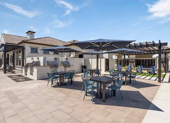 A patio with tables and chairs is shaded by umbrellas.