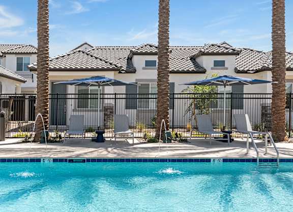 A pool surrounded by palm trees and lounge chairs.