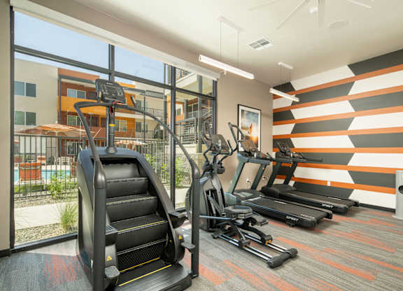 A gym with treadmills, elliptical machines and a striped wall.