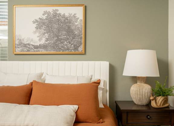 A bedroom with a bed, nightstand, lamp, and a picture on the wall.