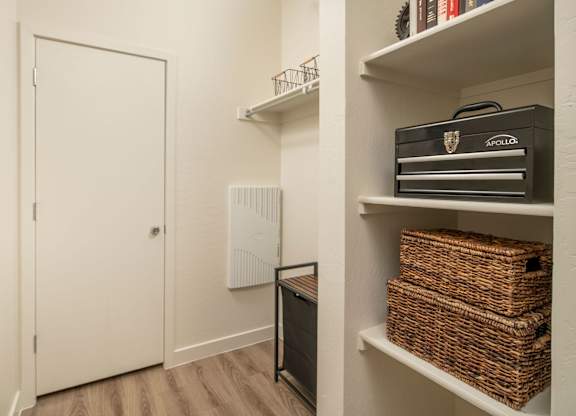 A white door is on the left and a shelf with baskets and a box is on the right.
