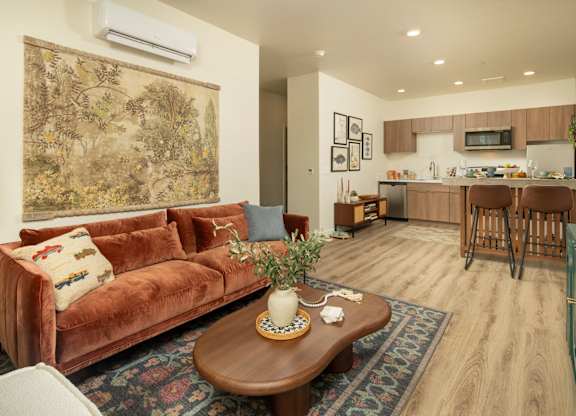 A living room with a brown couch and a coffee table with a vase on it.