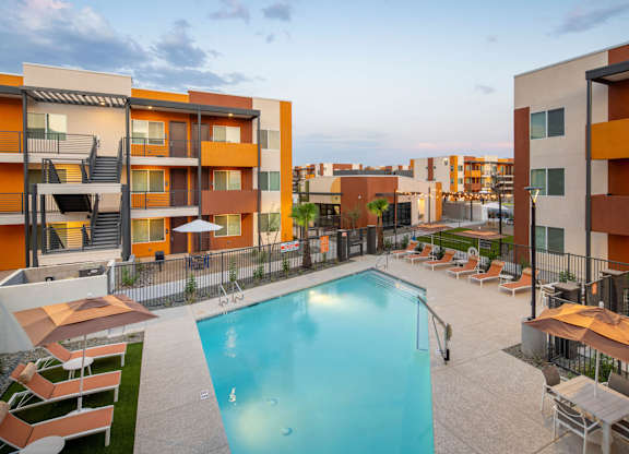 A swimming pool surrounded by lounge chairs and umbrellas in a residential area.