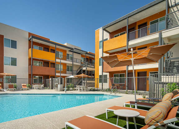 A modern apartment complex with a pool and lounge chairs.