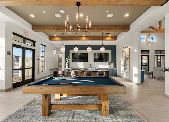 A pool table is in the middle of a room with a bar and a dining table.