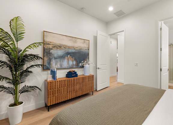 A room with a large painting on the wall and a bench with a potted plant on it.