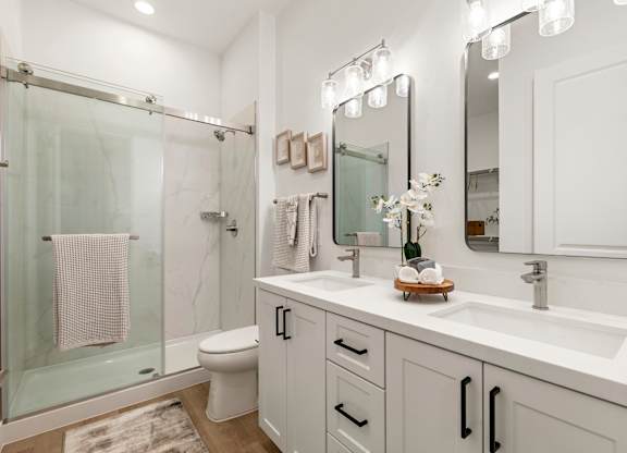 A white bathroom with a glass shower stall and a towel hanging on the glass door.