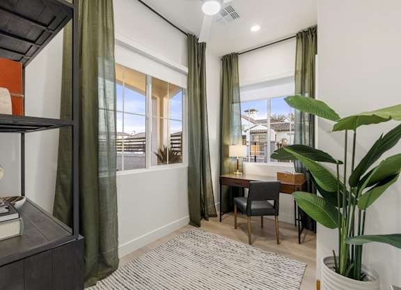 A room with a desk, chair, and a large window with green curtains.