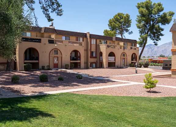 A building with arched doorways and windows is surrounded by a courtyard with a small tree in the center.