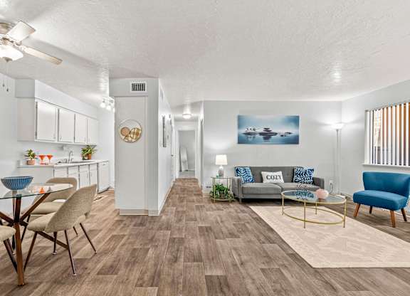 A living room with a grey couch, a blue armchair, a glass table and a wooden floor.