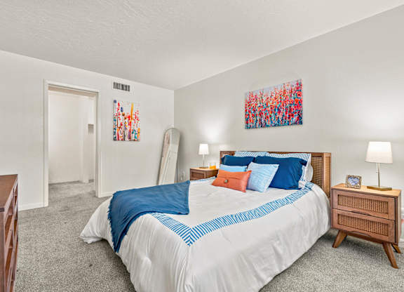 A bedroom with a bed, nightstand, and two paintings on the wall.